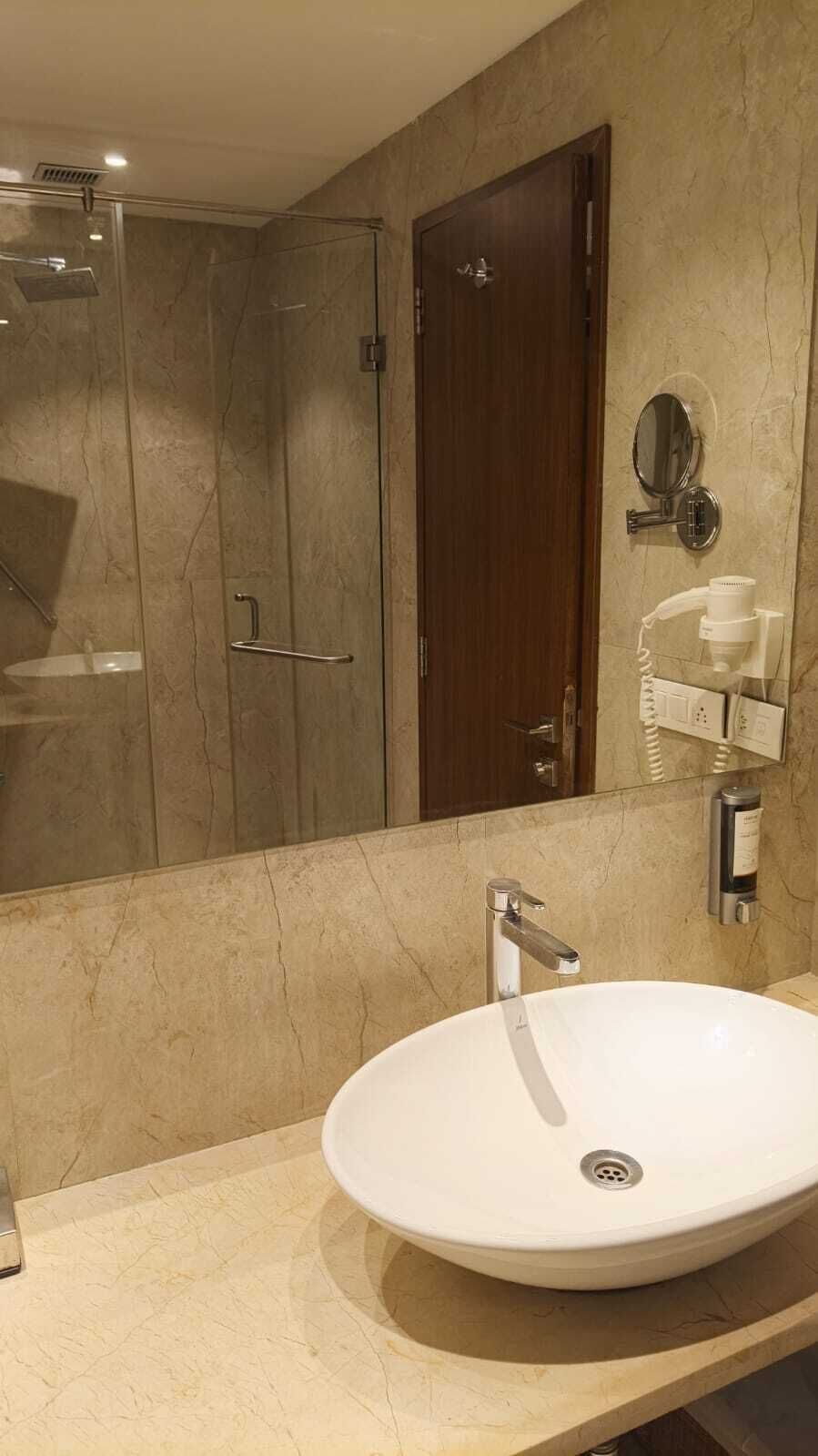 A bathroom with a white sink, a mirror, a shower, and a wooden door.