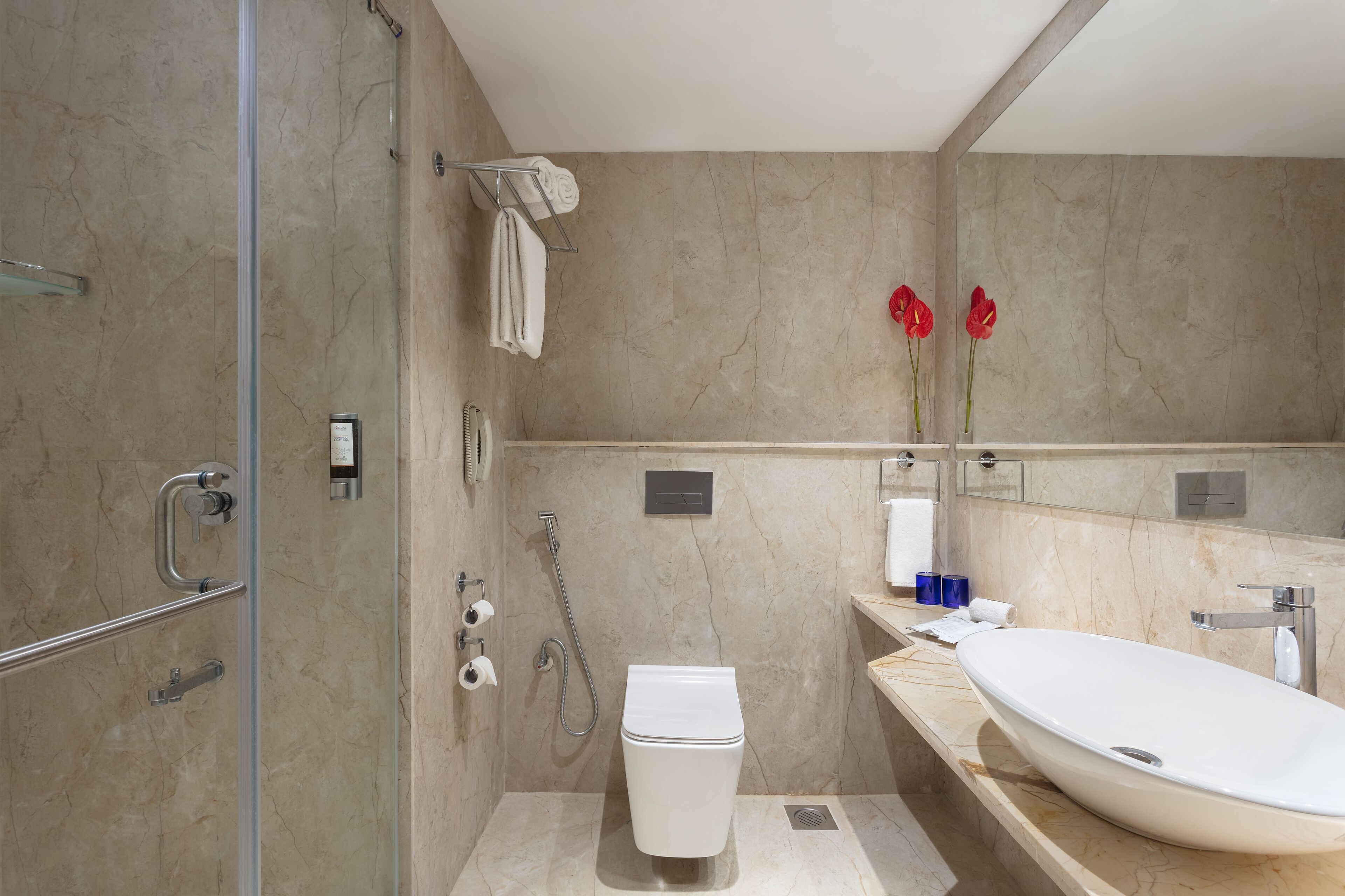 Un baño moderno con ducha a ras de suelo, inodoro, lavamanos y un espejo grande.