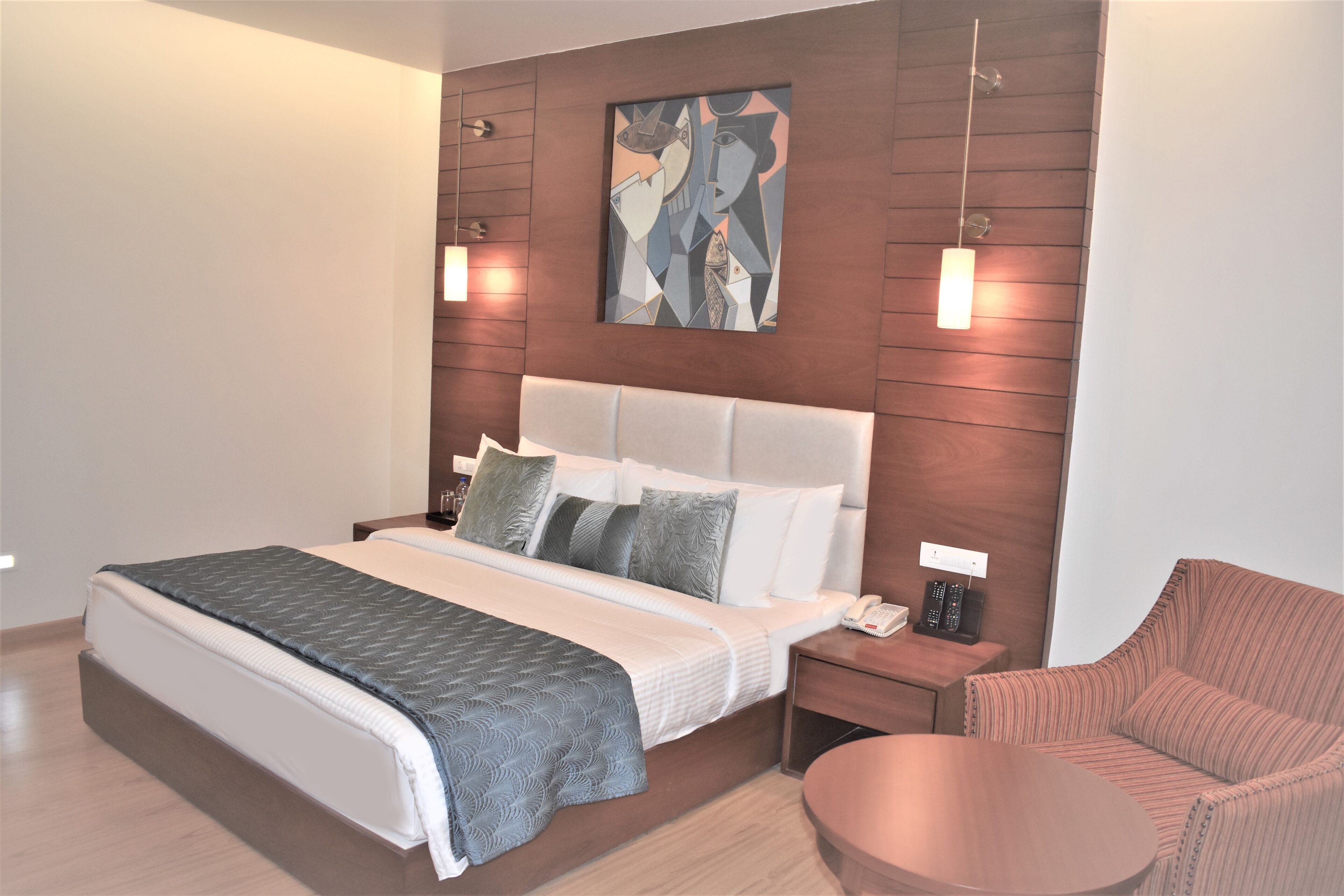 A modern hotel room with a large bed, bedside tables, a round table, and a painting on the wall.