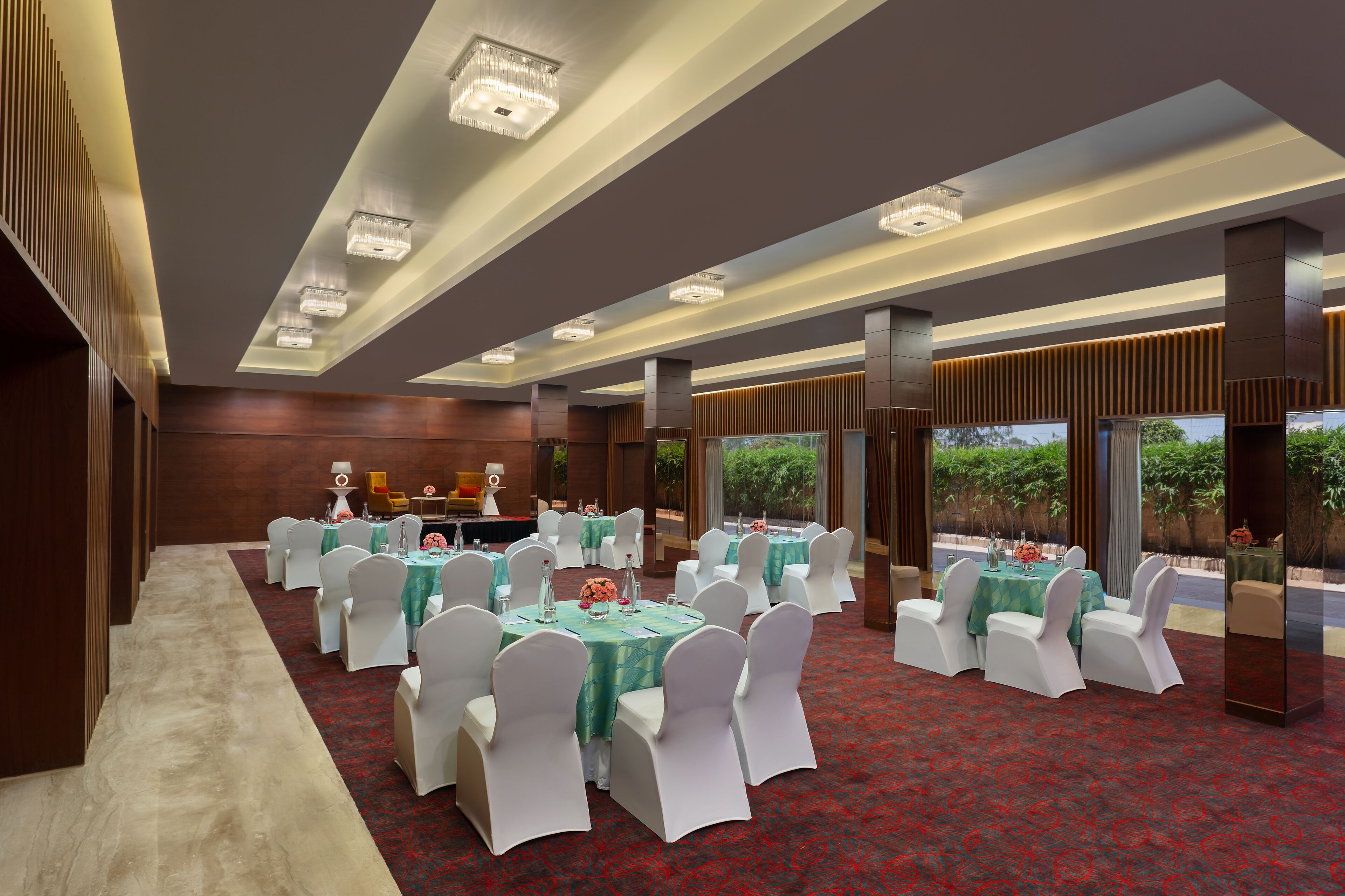 A banquet hall with round tables, white chairs, and a red carpet.