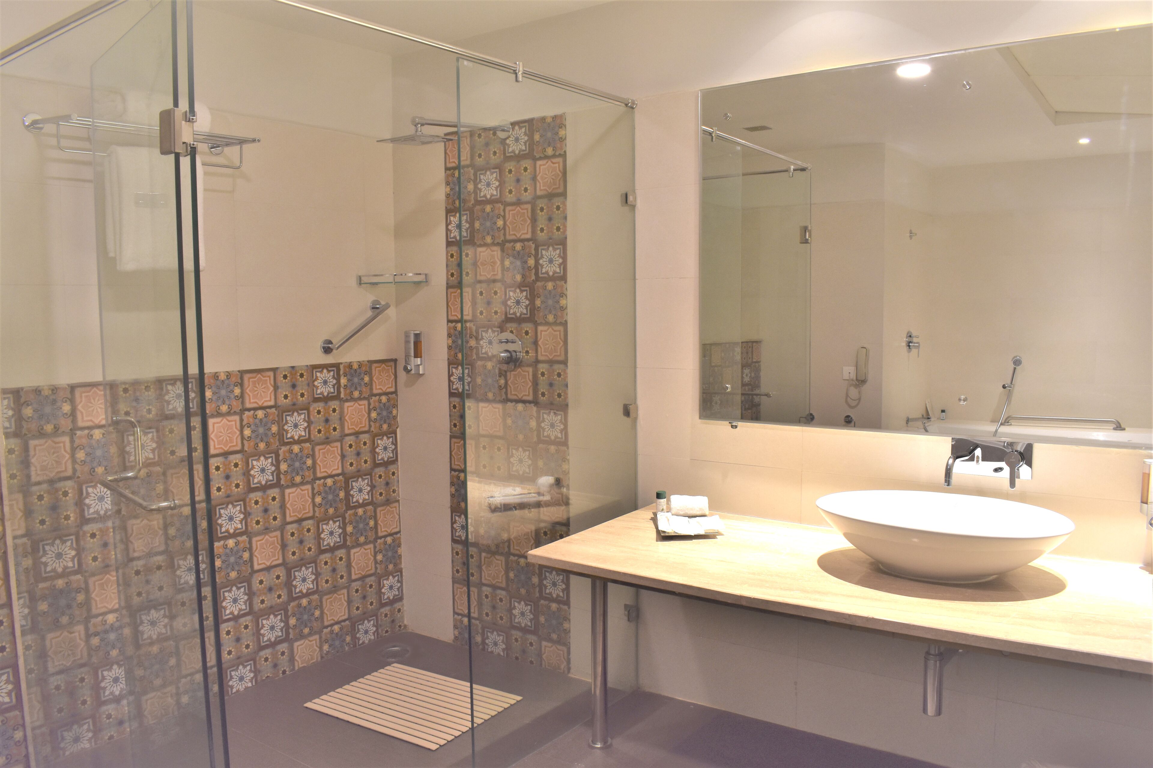 A modern bathroom with a glass shower enclosure, a large mirror, and a beige sink with a bowl.