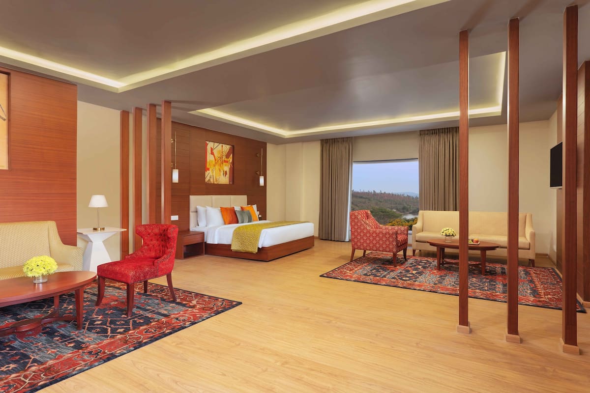 A hotel room with a bed, two seating areas, a TV, and a view of the outdoors.