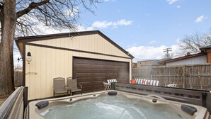 A hot tub area with a beige building and a brown garage door in the background. - HotTub PS5 GameRoom Theater PoolTable 420 (Denver)