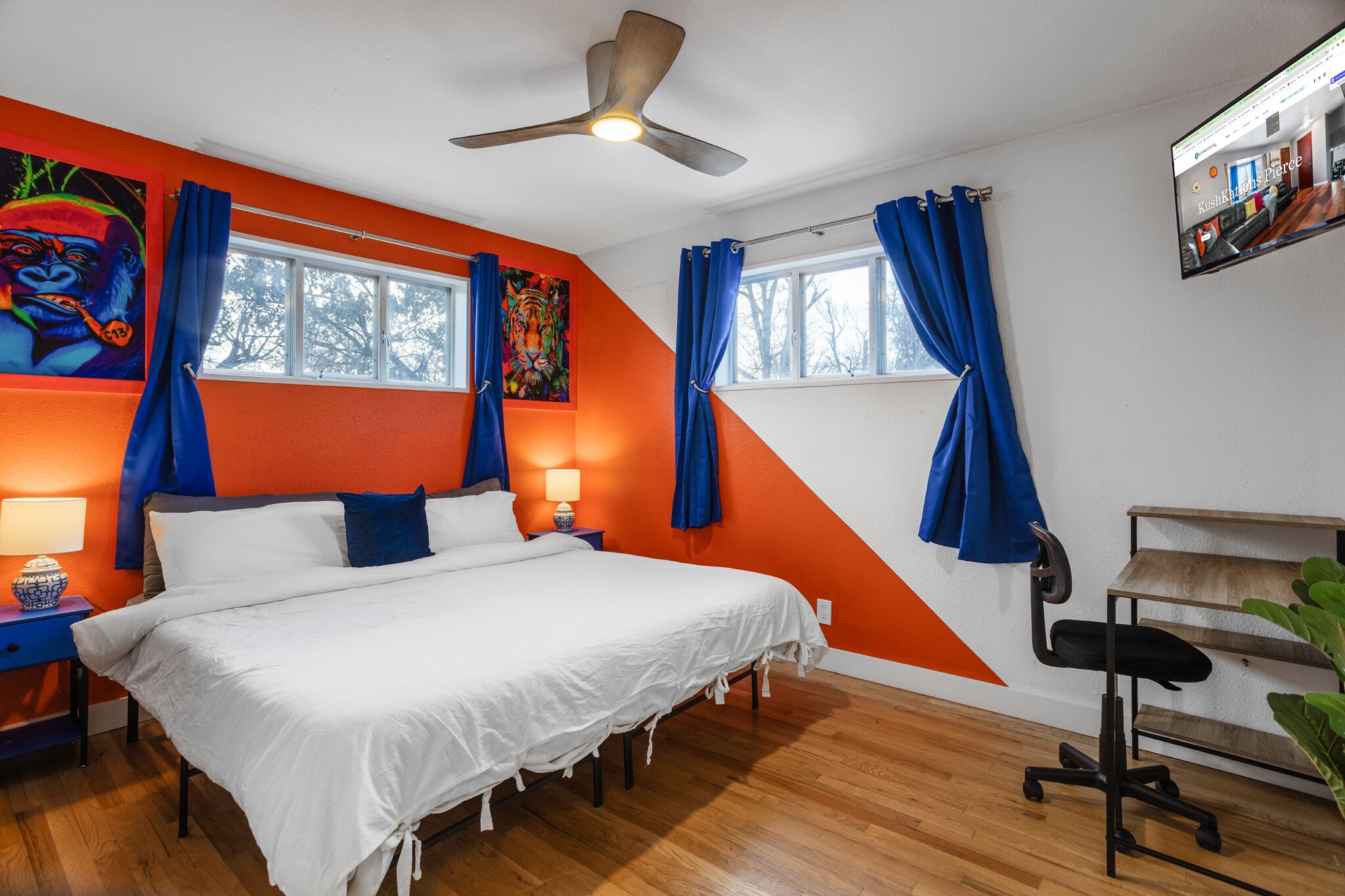 A bedroom with a bed, a ceiling fan, a TV, and a window with curtains.