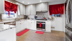 A modern kitchen with white cabinets, a stainless steel oven, and red curtains. - HotTub PS5 GameRoom Theater PoolTable 420 (Denver)