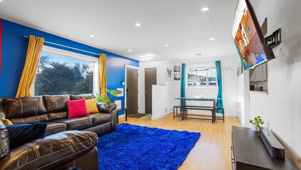 A modern living room with a leather sofa, a blue rug, and a flat-screen TV mounted on the wall. - HotTub PS5 GameRoom Theater PoolTable 420 (Denver)