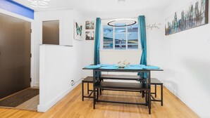 A dining area with a table set for four, a window with curtains, and wall art. - HotTub PS5 GameRoom Theater PoolTable 420 (Denver)