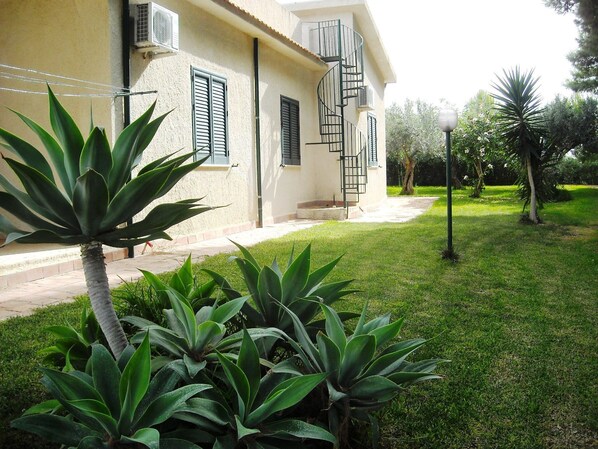 A building with a spiral staircase, air conditioning units, and a well-maintained lawn with agave plants.