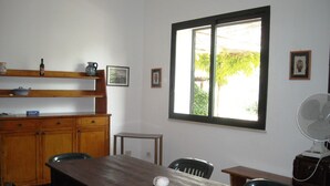 Ein Essbereich mit Holztisch, Stühlen, einem Ventilator und einem Fenster mit Blick auf Grünflächen.