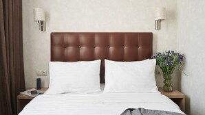 A hotel room with a brown headboard, white bedding, two bedside lamps, a nightstand with a phone and a magazine, and a vase with flowers. - Hotel Druzhba (Kyiv)