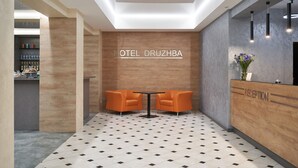 A reception area with a wooden reception desk, two orange chairs, a tiled floor, and a wall with the text "HOTEL DRUZHBA". - Hotel Druzhba (Kyiv)