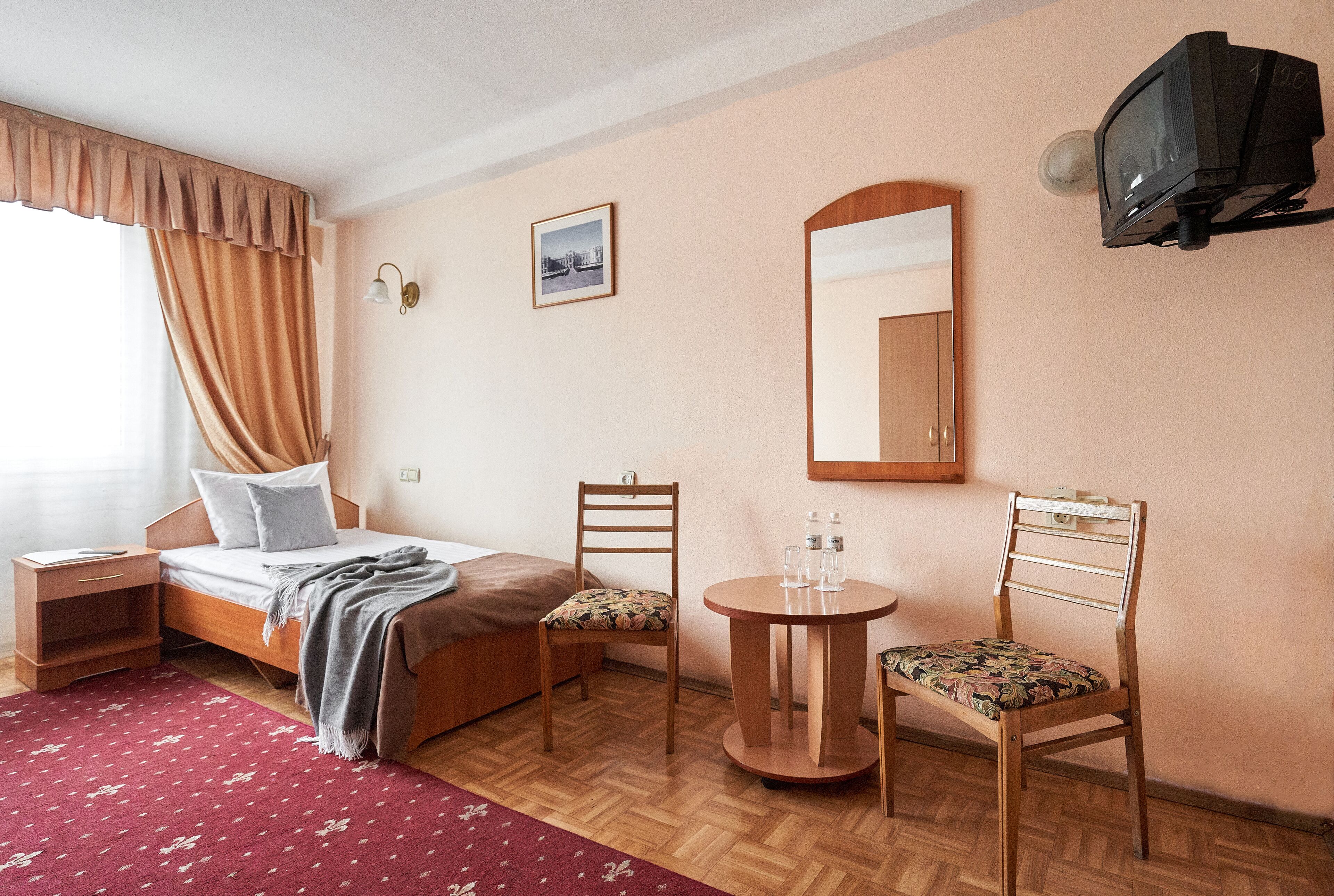 A hotel room with a bed, two chairs, a small table, a mirror, and a television.