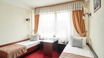 Habitación de hotel con dos camas individuales, un escritorio pequeño, un teléfono y una ventana con cortinas.