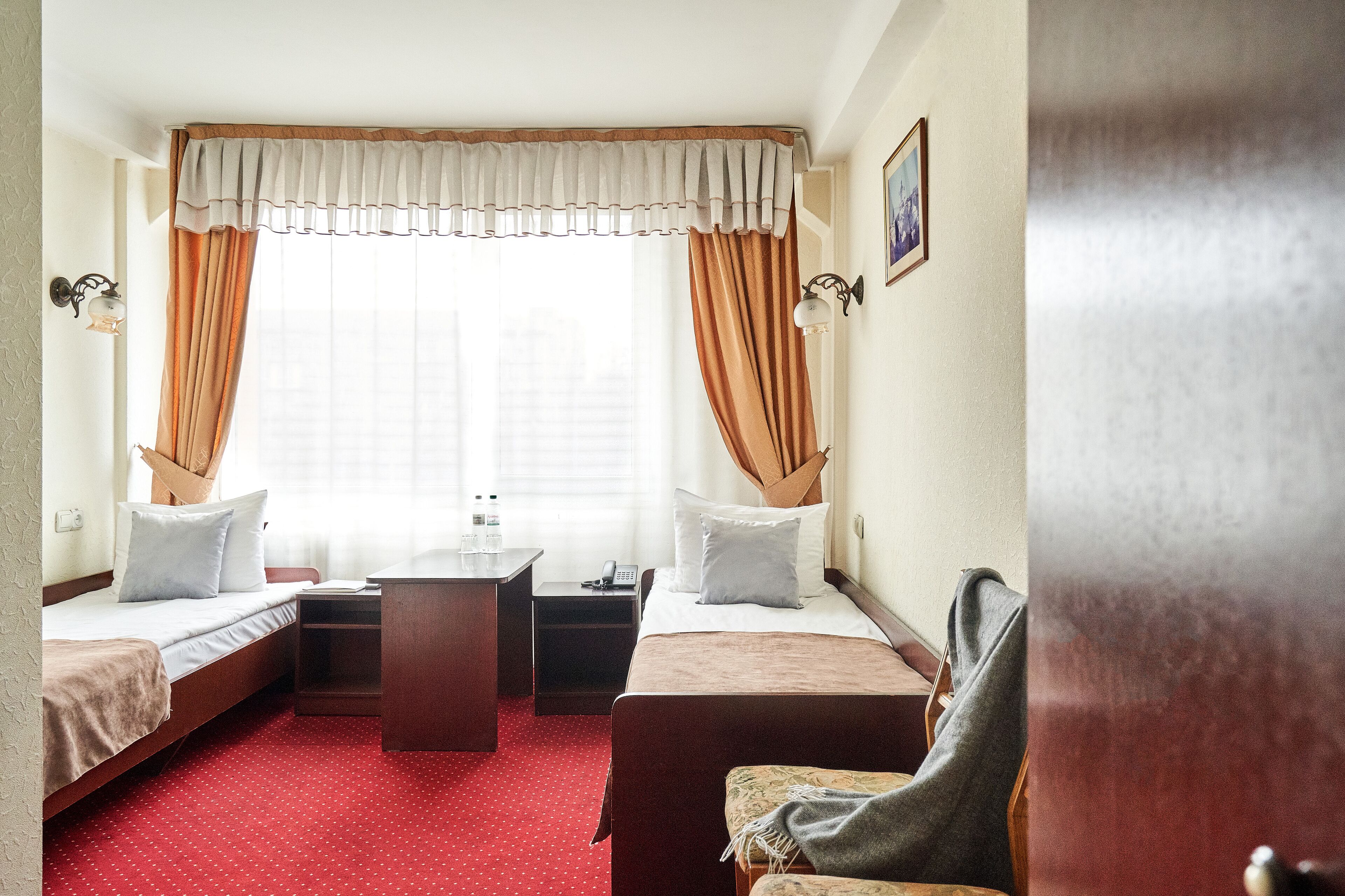 Una habitación de hotel con dos camas individuales, un escritorio pequeño, una silla y una ventana con cortinas.