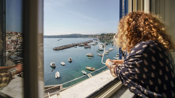Une vue depuis une fenêtre donnant sur un port, avec des bateaux et une côte lointaine.