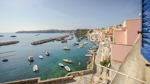 Une ville côtière où des bateaux sont amarrés le long du port, des bâtiments dotés de balcons donnant sur la mer et un ciel dégagé.