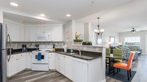 Una cocina moderna con armarios blancos, microondas, estufa y fregadero. Hay una zona de comedor con una mesa y sillas.