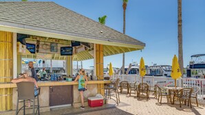 Un café frente a la playa con terraza y vistas a barcos al fondo.