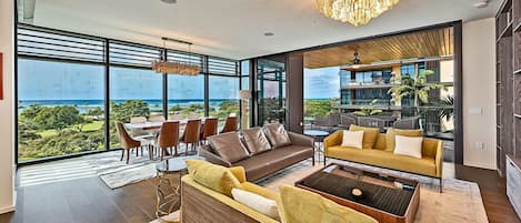 A spacious living area with a large window overlooking a lush landscape. There is a brown sofa, a yellow sofa, and a coffee table.