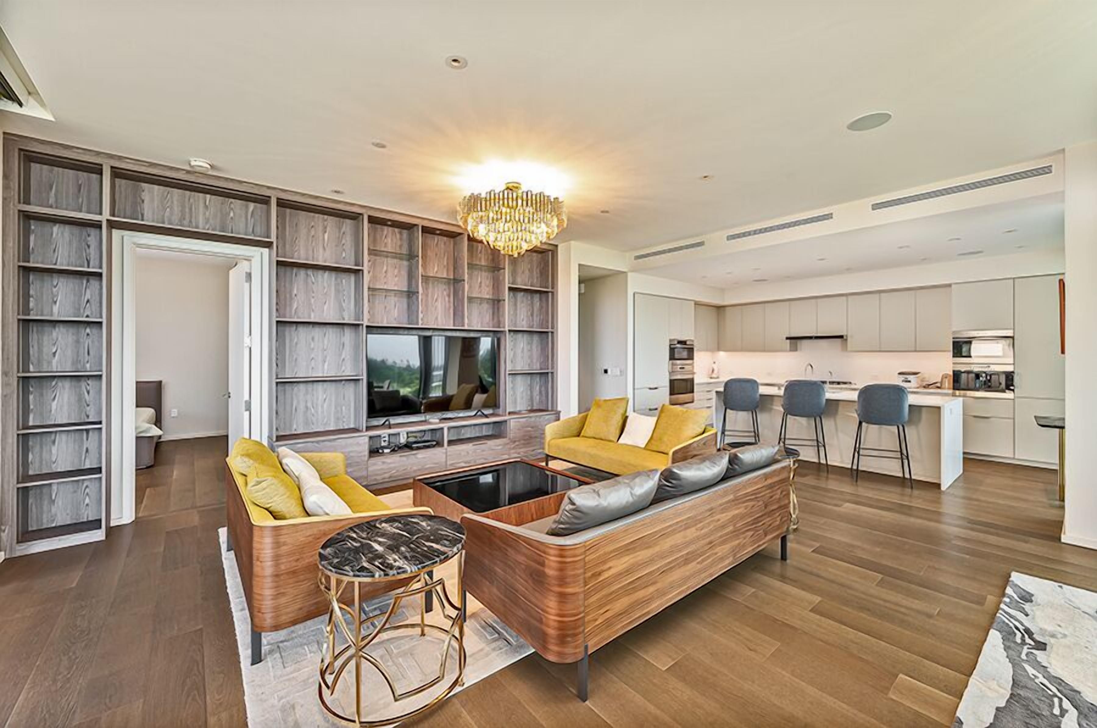 A modern living room with a sofa, coffee table, and TV, adjacent to a kitchen with bar stools.