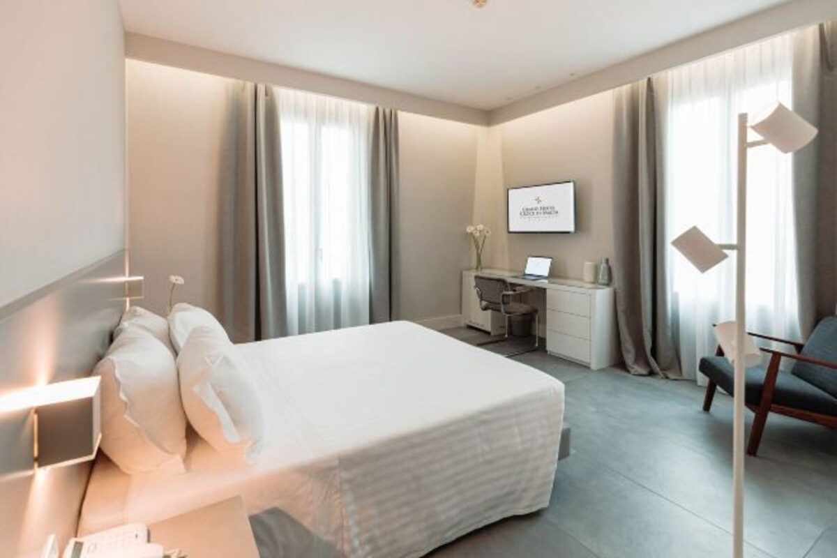 A hotel room with a bed, desk, chair, and a large window with curtains.