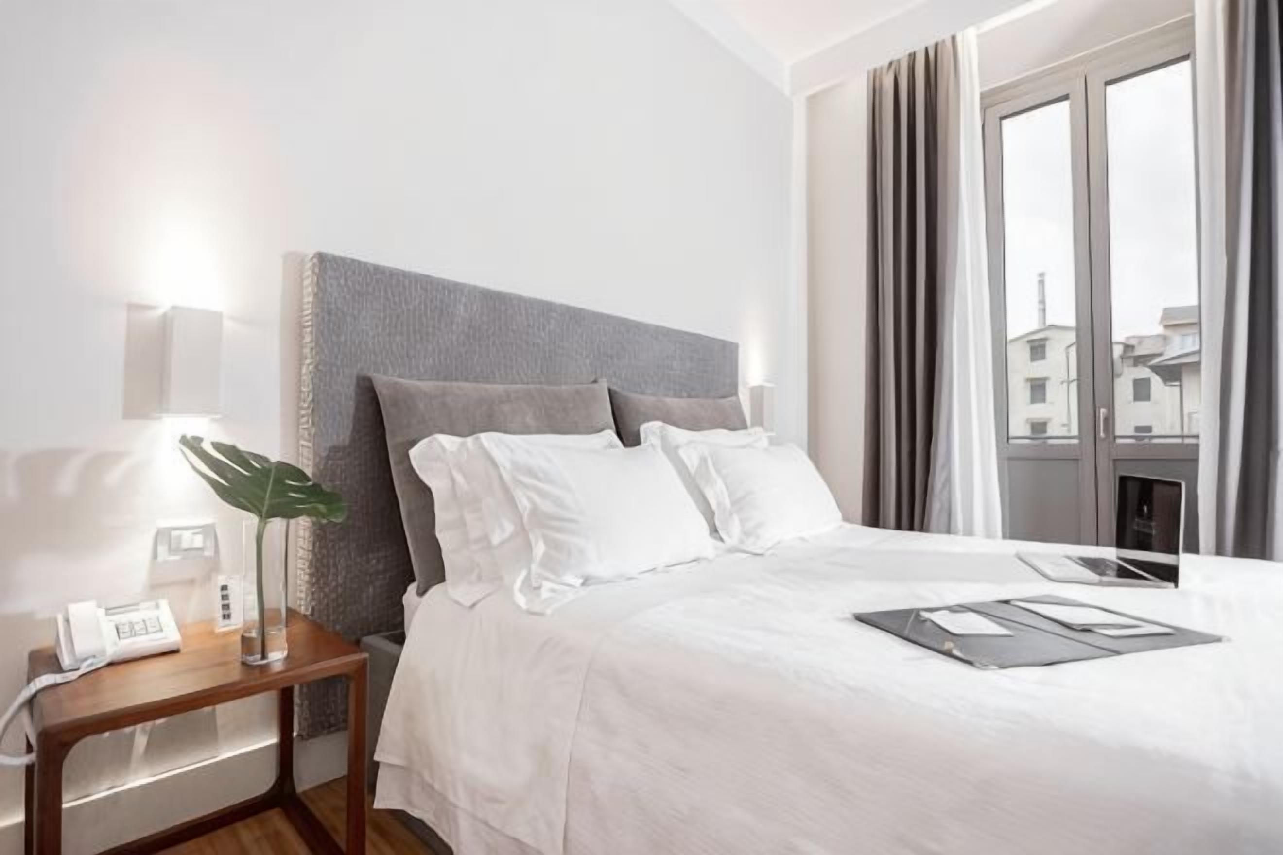 Une chambre d’hôtel avec un grand lit, une table de chevet avec une lampe, un téléphone et une fenêtre avec des rideaux.