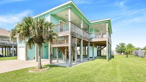 Une maison à deux étages avec un balcon, un palmier et un ciel d’un bleu éclatant.
