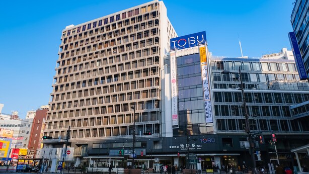 Et hotel med flere etager, et tydeligt 'TOBU'-skilt, et fodgængerfelt og en klar blå himmel.