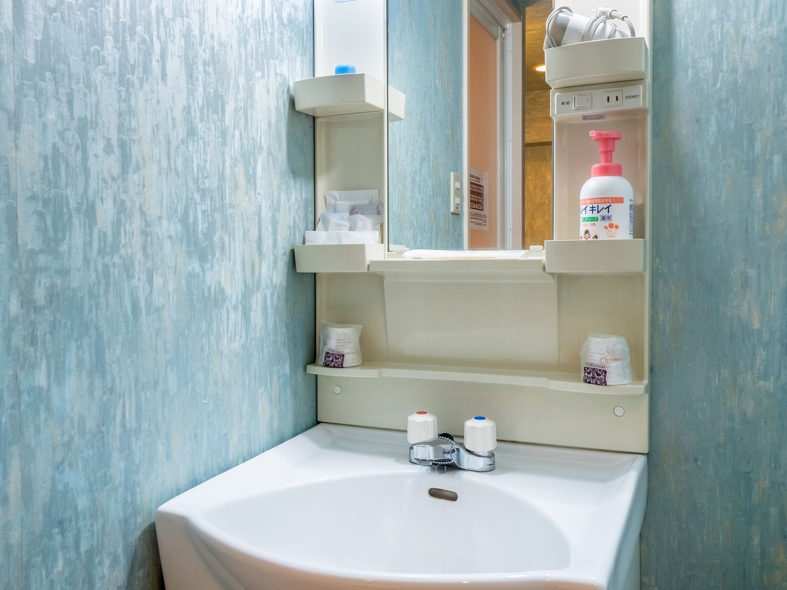 A bathroom with a white sink, a mirror, and shelves holding toiletries.