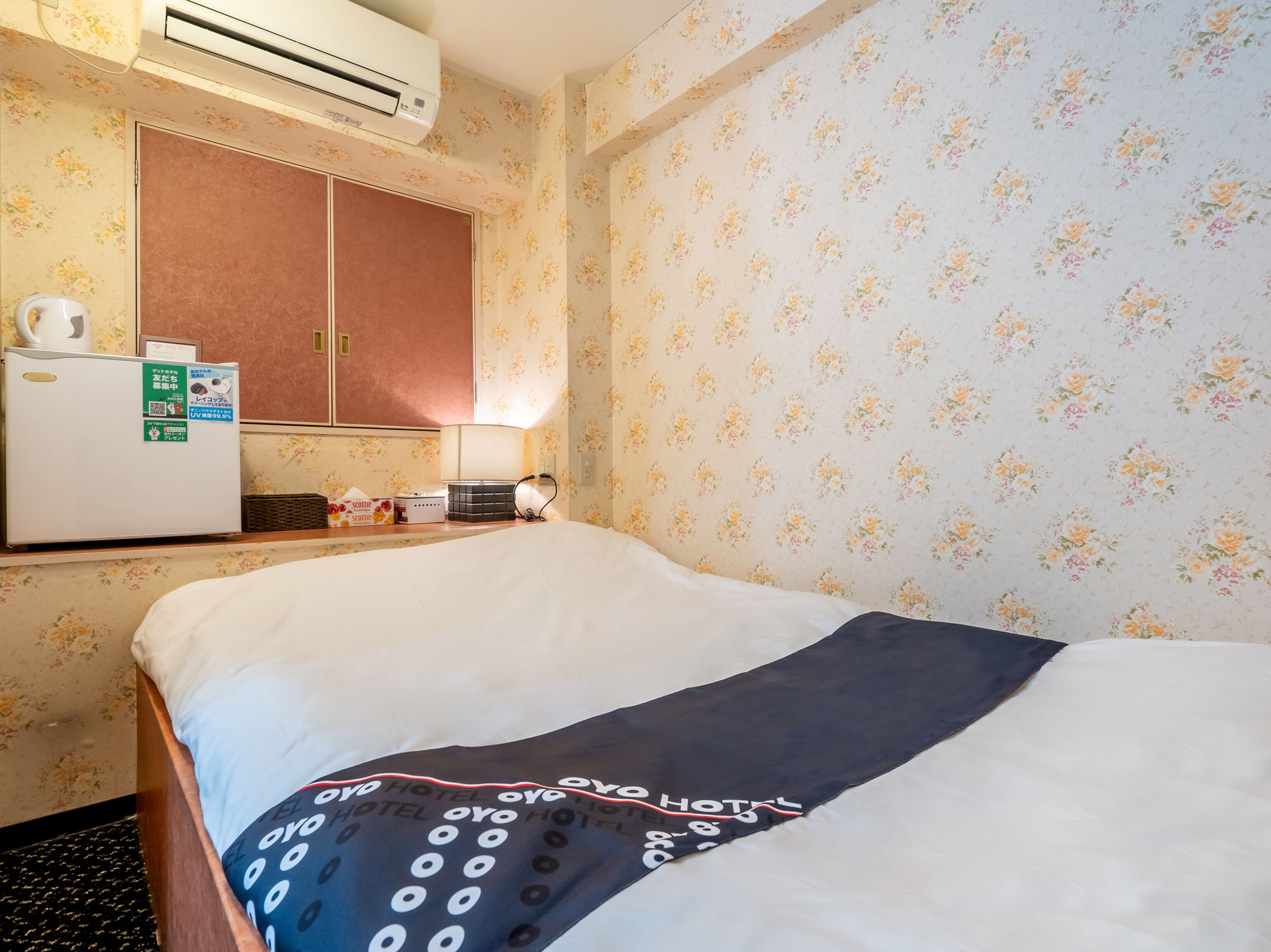 A hotel room with a bed, a small kitchenette, and floral wallpaper.