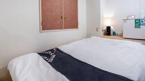 Et hotelværelse med seng, garderobeskab, aircondition, skrivebord med lampe og køleskab.