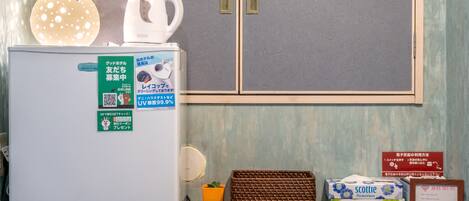 A hotel room with a refrigerator, a kettle, a basket, and flower boxes on the counter.