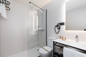 Un baño moderno con ducha envuelta en vidrio, un lavamanos blanco y un inodoro.