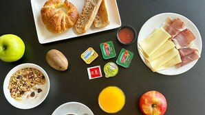 Een ontbijt met croissants, kaas, ham, appels, kiwi's en sinaasappelsap.