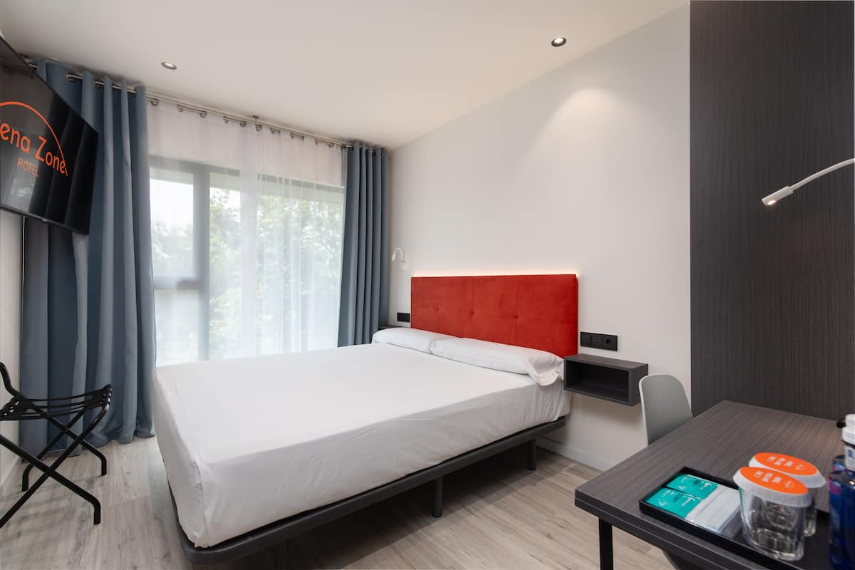 Una habitación de hotel con cama, escritorio, silla, televisión y ventana con cortinas.