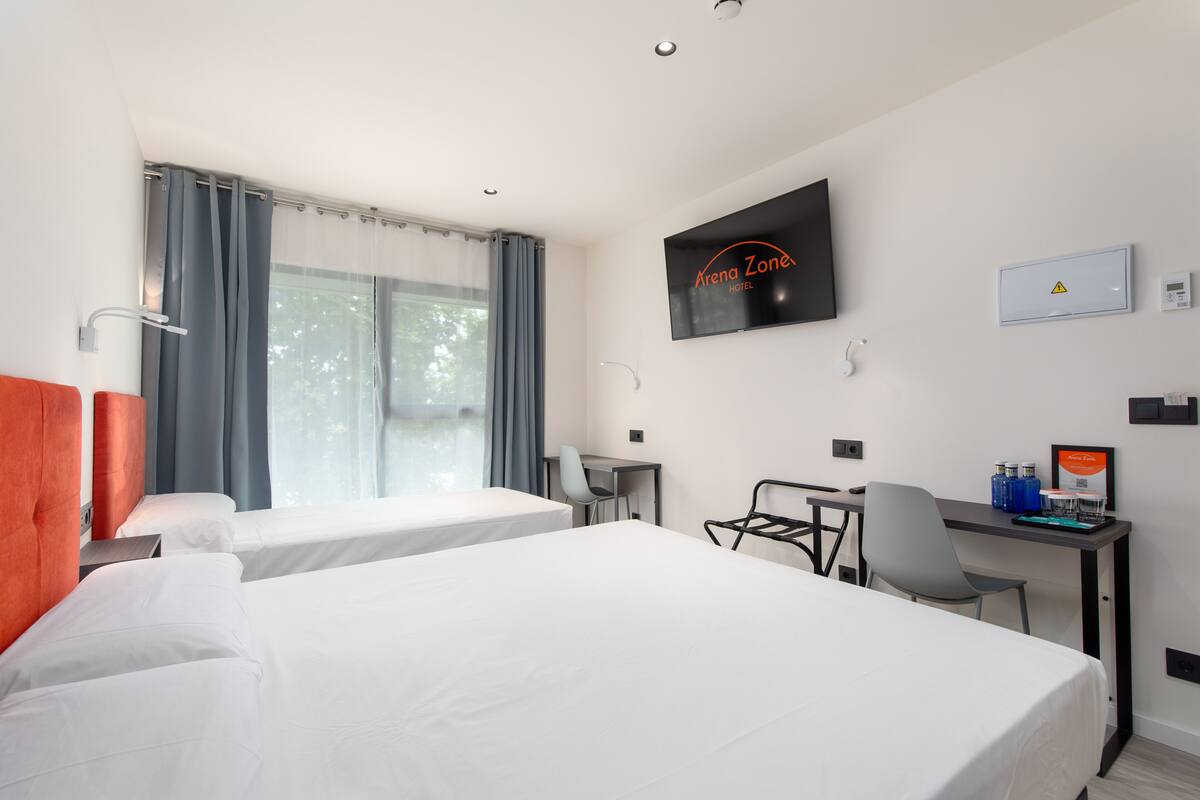 Habitación de hotel con dos camas, un escritorio, una silla, un televisor y una ventana con cortinas.