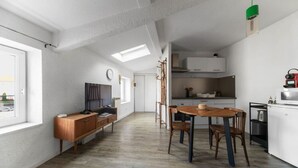 A spacious living area with a wooden dining table and chairs, a TV, and a built-in kitchen with white cabinets.