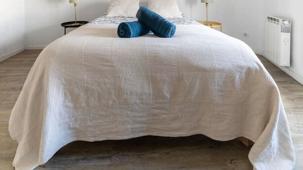 A minimalist bedroom with a large bed, two bedside tables, a wall-mounted light fixture, and two framed artworks.