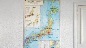 A room with a large map of Japan on the wall, a beige armchair, and a small round table with a black top.