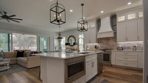 Une cuisine moderne avec des meubles blancs, un îlot central, des appareils en acier inoxydable et des luminaires suspendus.