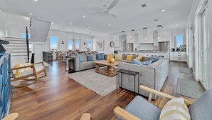 A spacious living area with a large sofa, a coffee table, and a dining table. There is a kitchen area with modern appliances and cabinets. - Another Round by GSVR | Beachfront w/ Pool & Elevator | Free Activities/Golf (Gulf Shores)