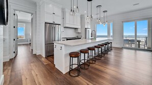 A modern kitchen with white cabinetry, stainless steel appliances, and a bar area with stools. - Another Round by GSVR | Beachfront w/ Pool & Elevator | Free Activities/Golf (Gulf Shores)