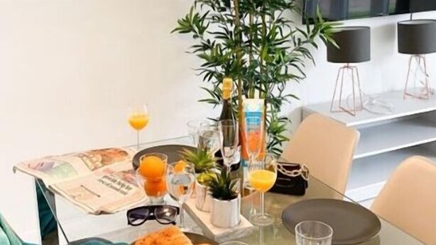 A dining table with a newspaper, glasses, a plant, and a handbag. - Tudors eSuites Luxury House Garden (Birmingham)