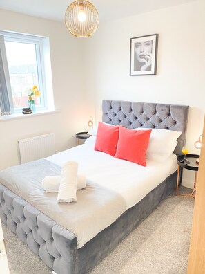 A neatly made bed with white and red pillows, a grey upholstered headboard, and a white duvet. - Tudors eSuites Luxury House Garden (Birmingham)
