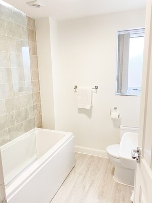 A bathroom with a bathtub, toilet, and a window with curtains. - Tudors eSuites Luxury House Garden (Birmingham)
