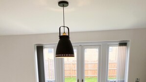 A modern living room with a round coffee table, a sofa, and a large window with a view of a backyard. - Tudors eSuites Luxury House Garden (Birmingham)