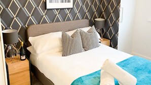 A neatly made bed with a blue blanket, a framed picture on the wall, and a hanging light fixture. - Tudors eSuites Luxury House Garden (Birmingham)