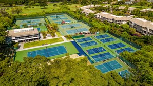 An aerial view of a golf course with multiple tennis courts, surrounded by lush greenery and residential buildings. - Private and Sweet Wailea 1 BD+2 BA Grand Champions Villa (Wailea)