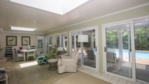 A sunlit room with a dining area, a comfortable seating area with a chair and ottoman, and a view of a swimming pool through large glass doors. - 4 Bedroom Pinehurst Home with Pool and Hot Tub (Pinehurst)