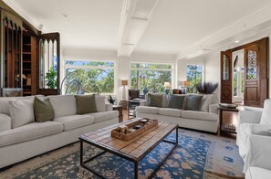 A spacious living room with two sofas, a coffee table, and a view of the outdoors through large windows. - Stunning home close to the Ocean Course (Johns Island)